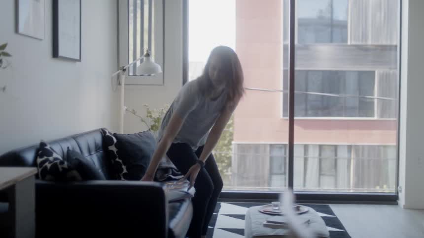 A woman is sitting down and opening a laptop on her couch during the day