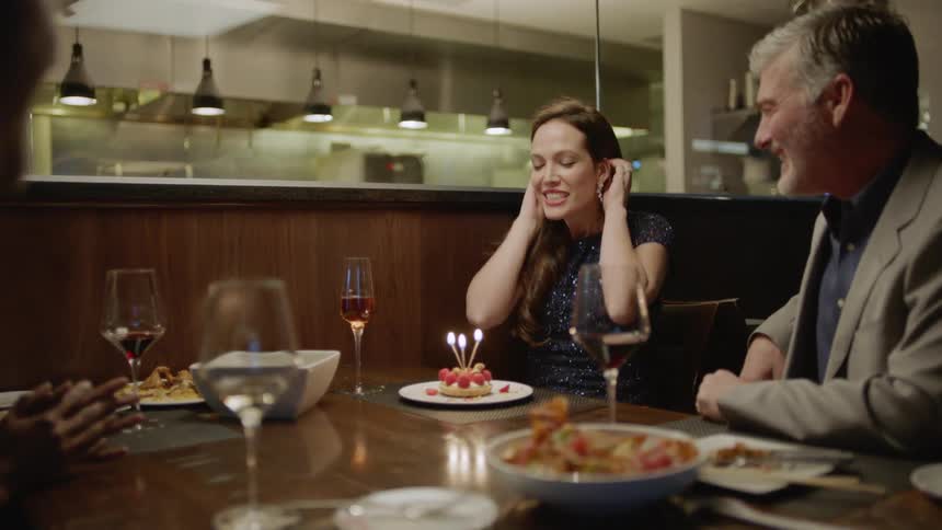 A woman blows out the candles on a dessert and gets a kiss