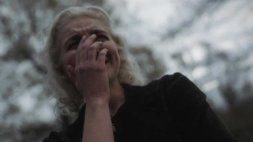 Woman cries outside near trees on a cloudy day