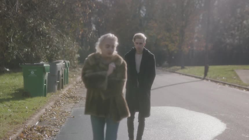 Woman walks down a deserted street with a man following behind