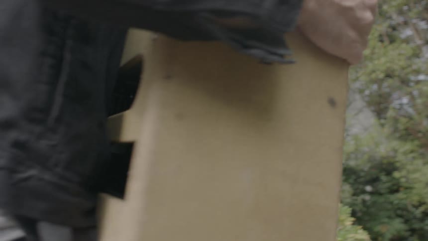 Man lifts a heavy object and carries it towards a building