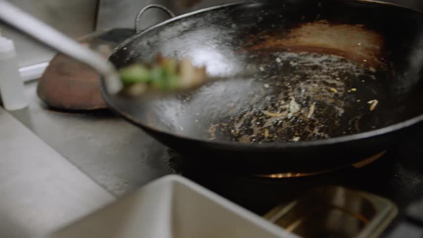 A chef takes food out of a wok and plates it