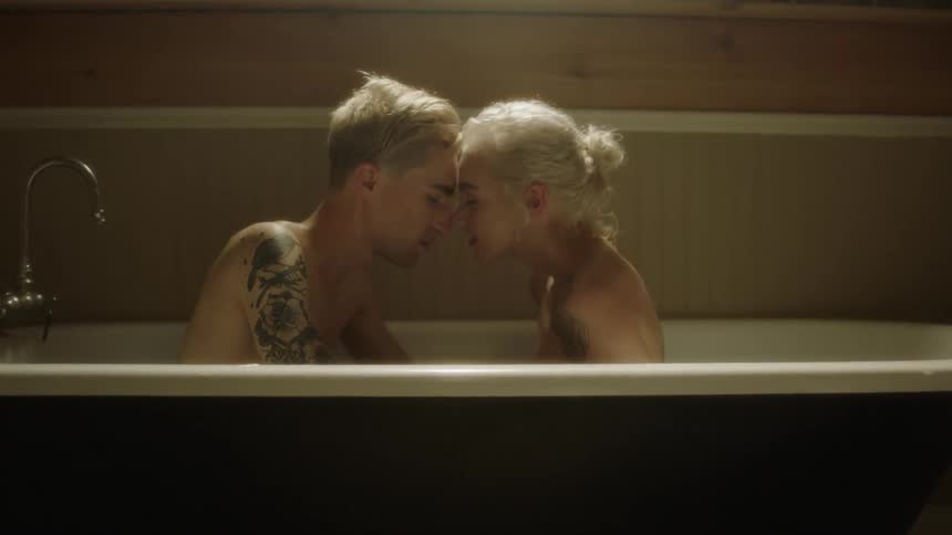 Man and woman sit in a bathtub and kiss