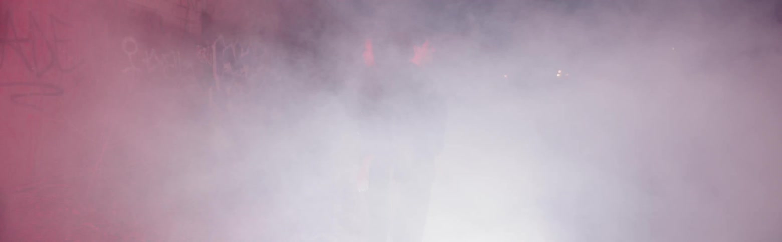 Two people stand in smoke outside at night