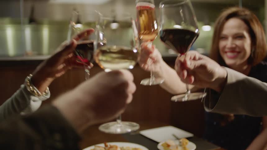 Four people sitting at a restaurant clink glasses together