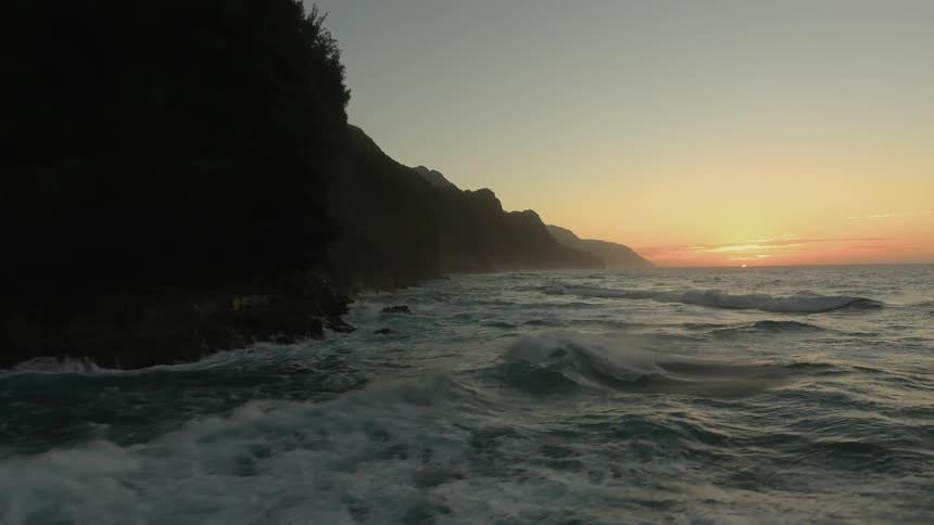 Ocean waves splash against the shore at sunset