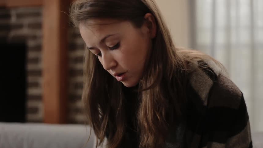 A teenage girl is sitting on a couch writing in a notebook and talking in daylight
