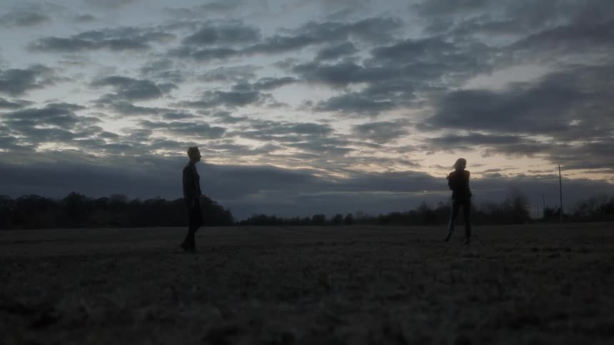 Person walks in a field at sunset to meet another person