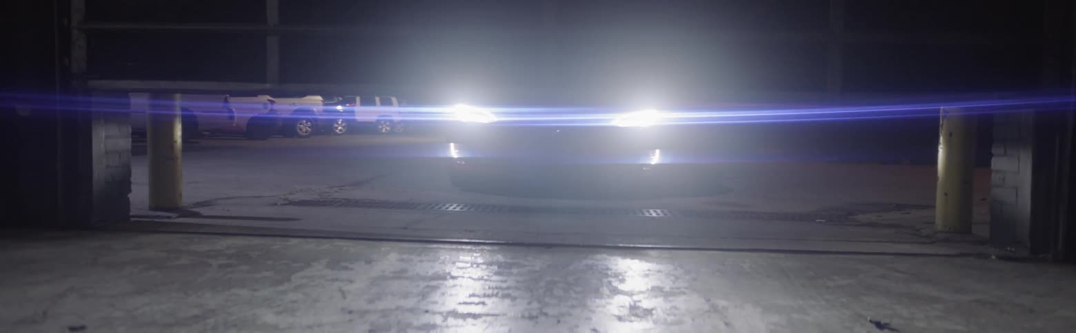 A garage door goes up to reveal a car with headlights on waiting outside