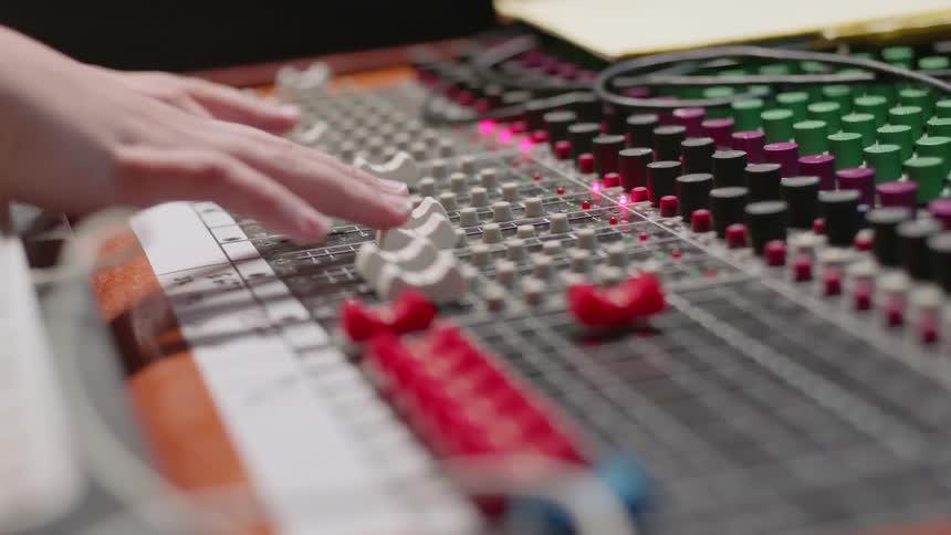 A woman is adjusting sliders on a sound mixer inside a studio