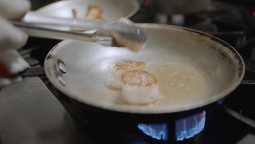 A man cooks scallops in a skillet