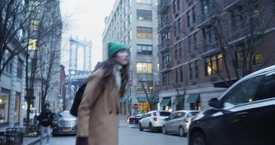 A woman is crossing a street in a city at dusk