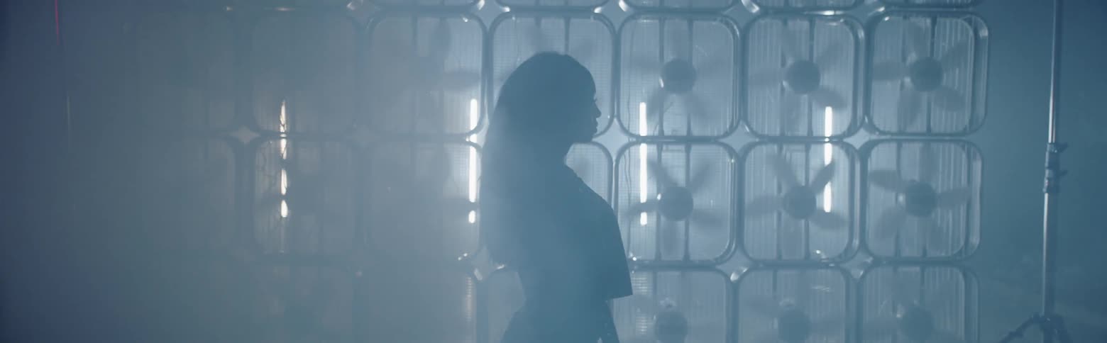 A woman stands in profile in front of a wall of box fans