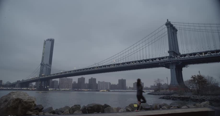 Woman jogs near water with a bridge over it