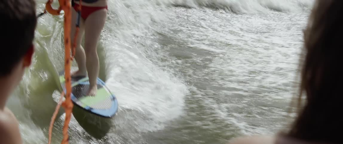 A woman rides on a surfboard pulled by a boat