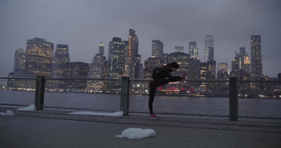 Woman stretching on fence in front of city skyline at night
