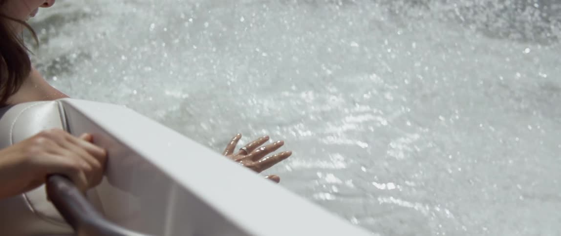A woman is dragging her hand over the water as she rides in a boat in daylight