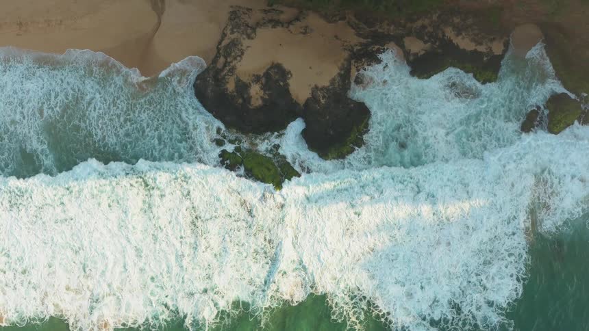 Oceans waves break and splash as they come to shore on a sandy beach