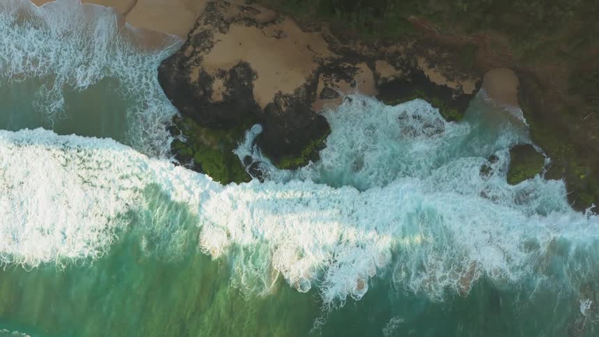 Waves are crashing against rocks on a beach during the day