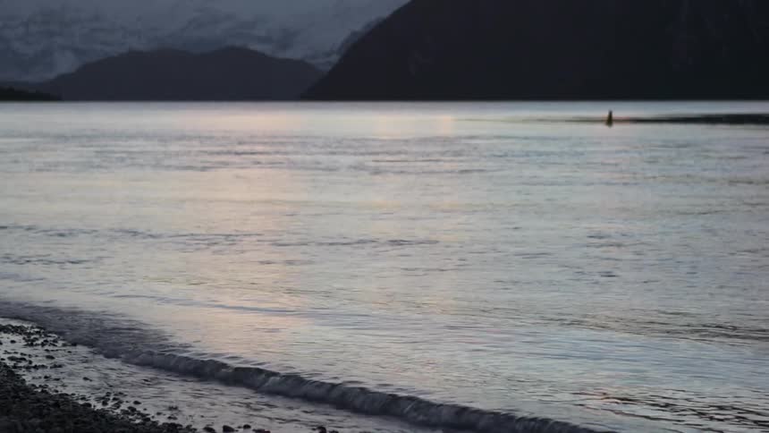 Waves lapping on shore with snow covered mountains in the background