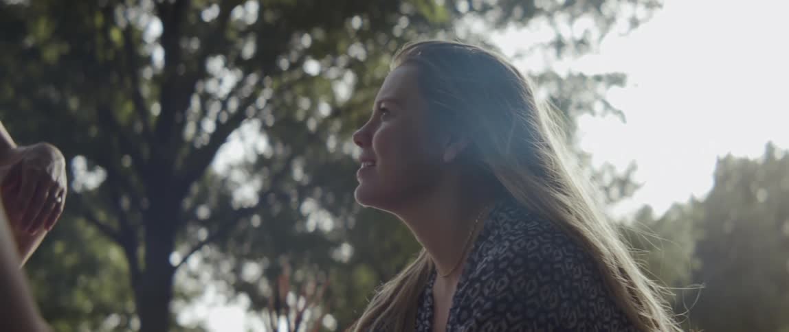 Blond woman smiles as she sits near the trees