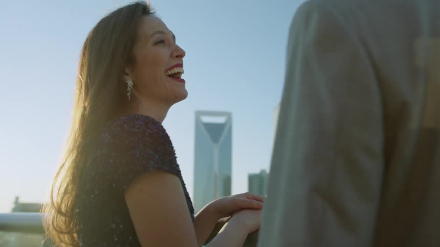 A woman smiles and laughs as she talks to a man on a roof deck