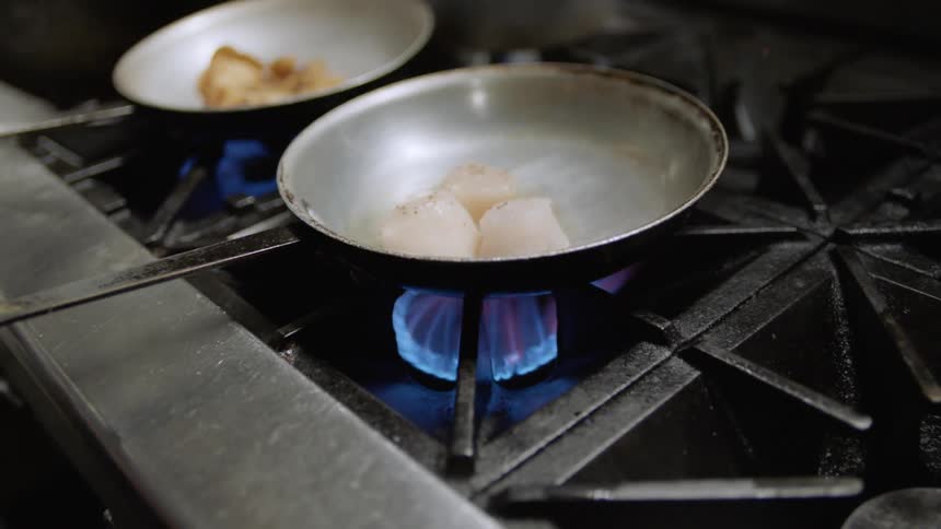 A chef shakes a pan with food in it cooking on a stove