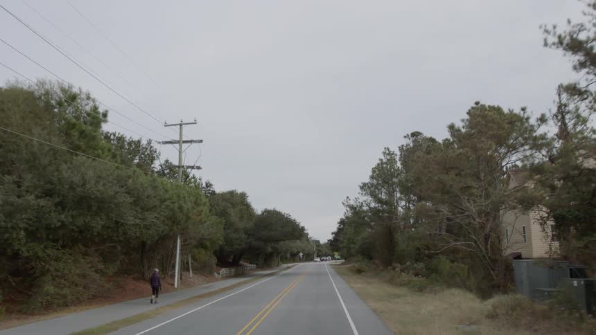 A person walks on the side of the road as cars travel on it