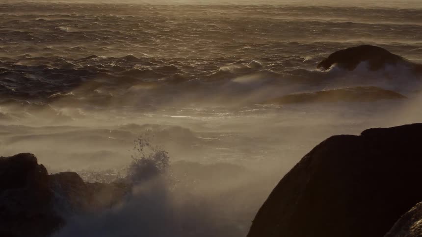 The heavy waves crash against the shore at sunset