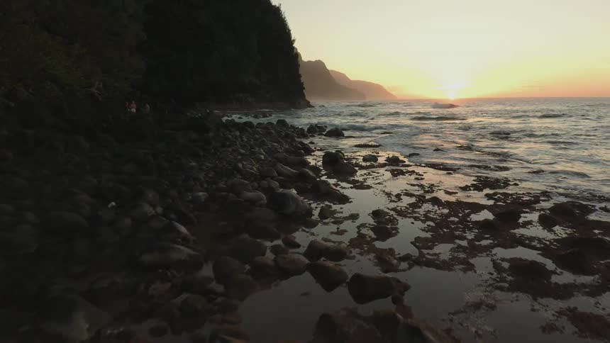 The sun shines as the tide flows towards the rock covered shore