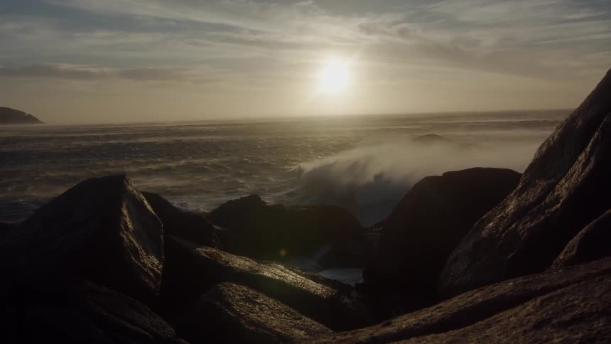 Sun sets over a body of water splashing up on rocks
