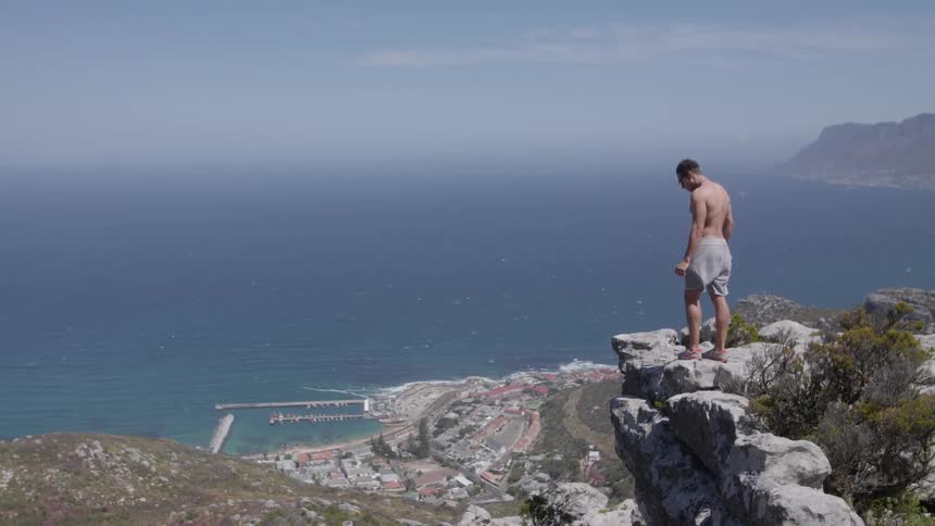 Man stands at the edge of a cliff looking down to a large body of water