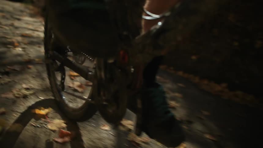 Close up of someone's feet as they pedal a bicycle on a leaf-strewn path
