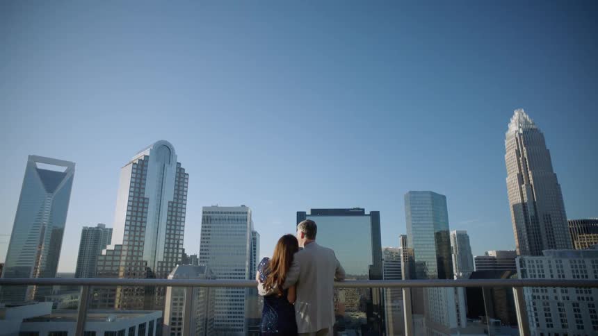 A man and woman embrace atop a building looking out onto the skyline