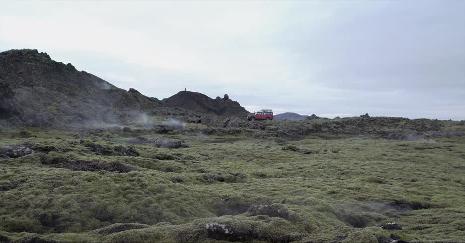 Steam is billowing from fissures in the ground in a natural landscape where a vehicle is parked