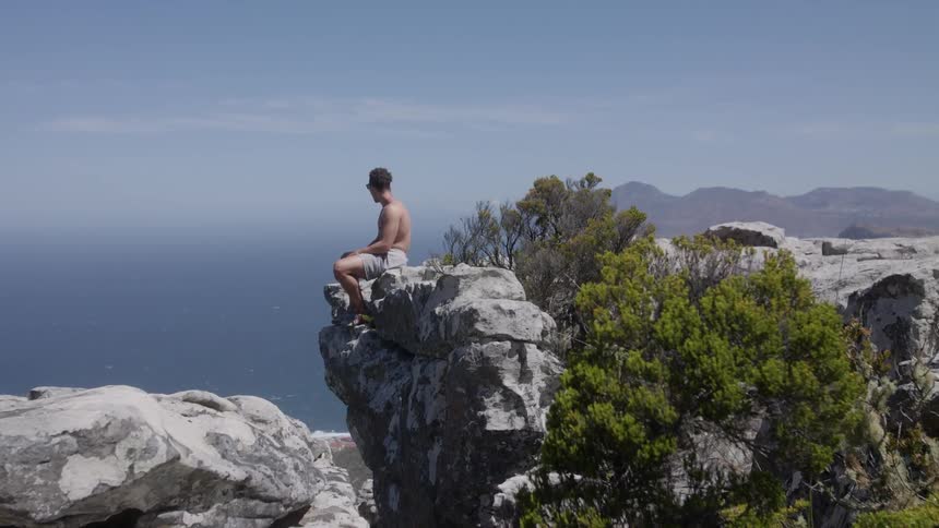 Man sits on a large rocky cliff overlooking a body of water