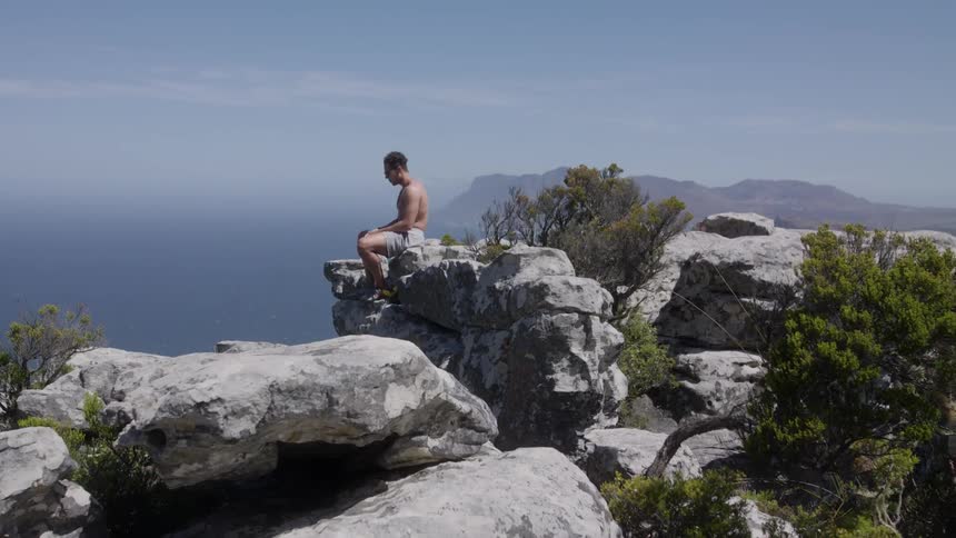 A man sits on a rock on the cliff shore