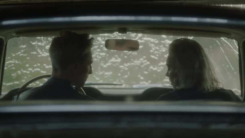 A man and woman sit in the front seat of a car as its drenched in water