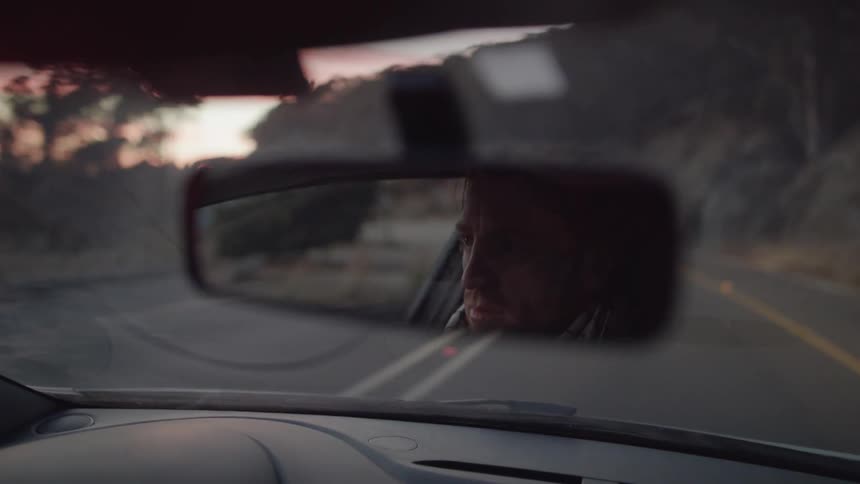 A man is driving on a rural road at sunset