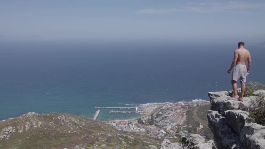 Man wearing shorts stands on the rocks overlooking the ocean