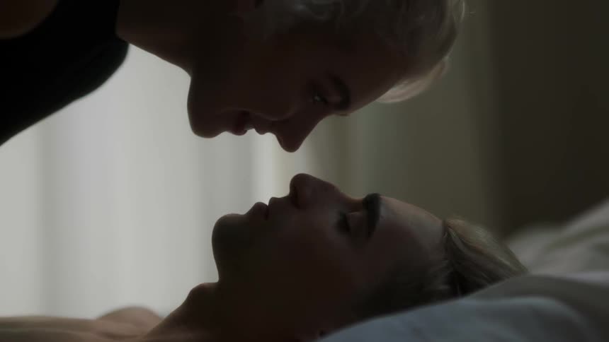 A woman leans in close to a man laying in bed