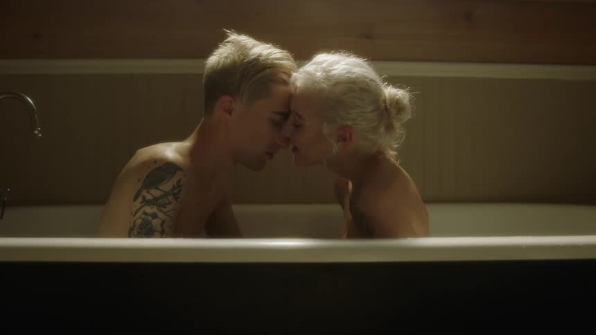 A man and woman sit up in a tub and rub noses