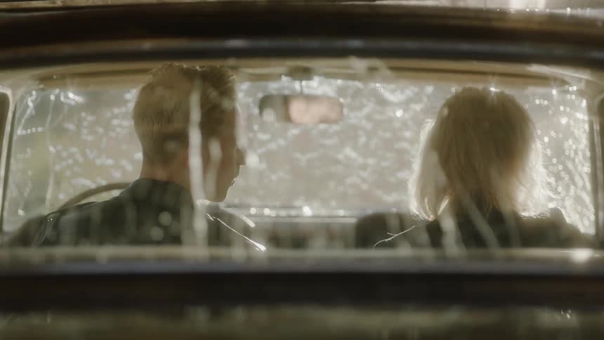 A couple sits in a car as water pours down on it