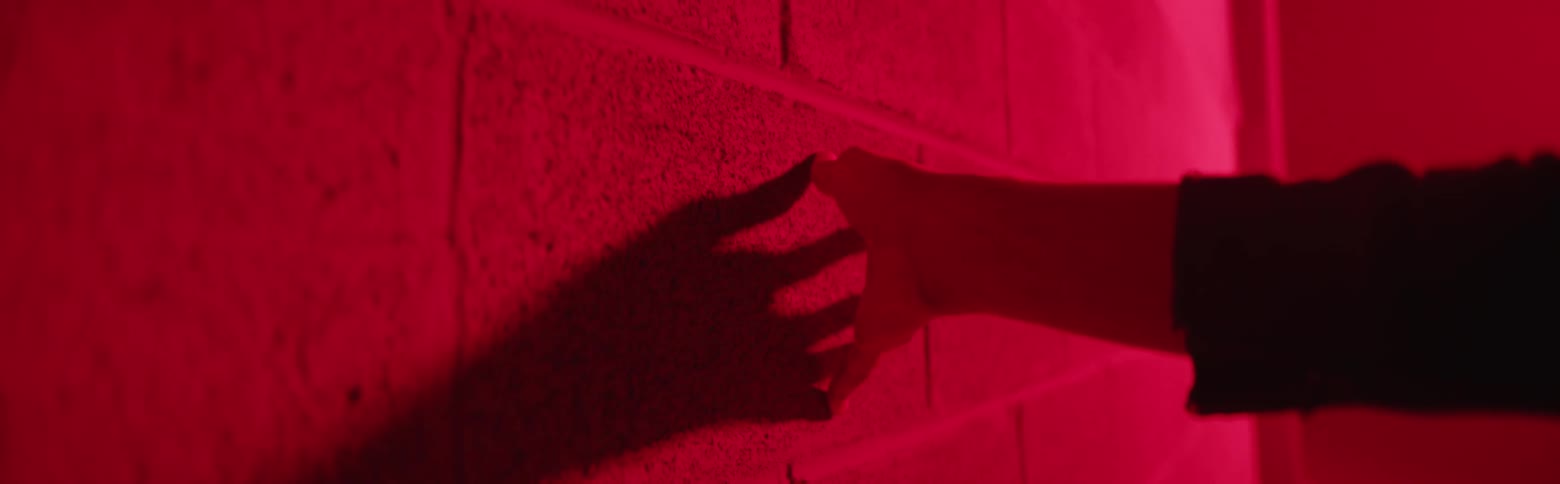 A person drags their hand over a cinder block wall in a red light