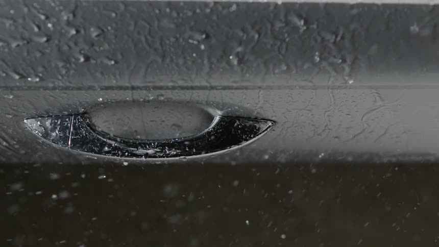 Rain pelts down on a car door and handle