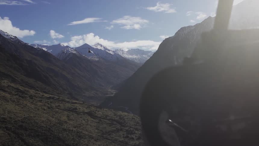 Two helicopters face each other in the air between some mountains