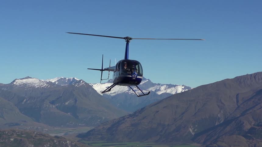 A black helicopter lifting off in front of snow covered mountains