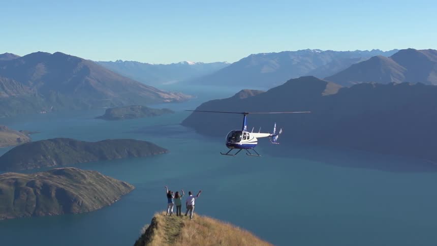 Helicopter flies up to some people standing on the tip of a mountain