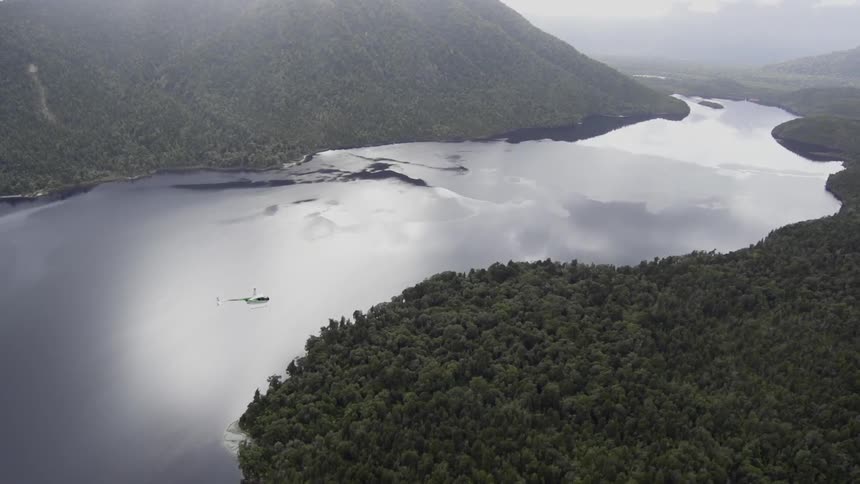 A helicopter flies over a smooth mountain lake