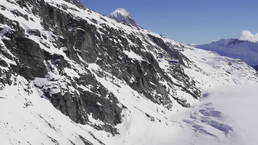 Helicopter flies by the side of a snowy mountain